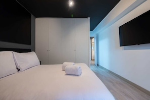 Ein modernes Hotelzimmer mit einem großen Bett, weißen Laken, einem Schrank und einem flachbildfernseher an der Wand.