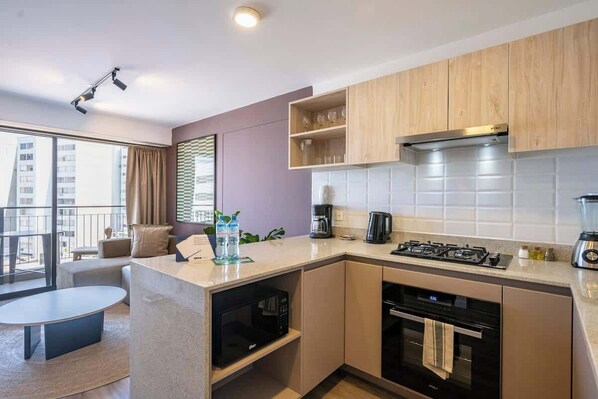 A modern kitchen with a gas stove, oven, and microwave, wooden cabinets, and a large window with a view of buildings.