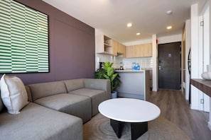 A modern living room with a sofa, a round table, and a kitchen in the background.
