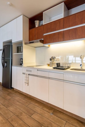 Una cocina moderna con armarios blancos, un refrigerador de acero inoxidable, alacenas de madera y una encimera con un lavamanos y un escurreplatos.