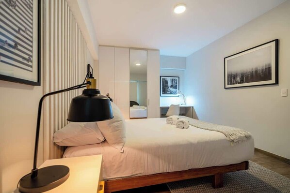 A modern hotel room with a bed, bedside lamp, and a mirror.