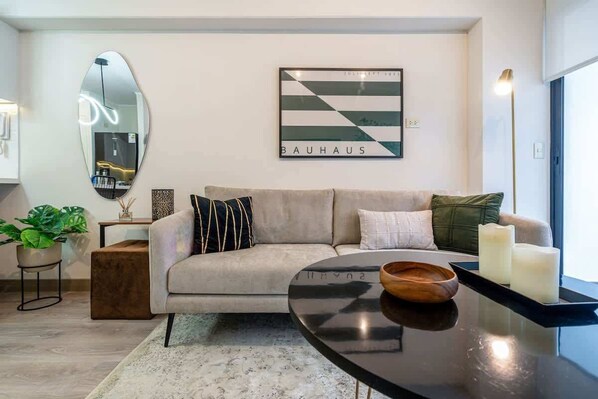 Ein modernes Wohnzimmer mit einer Couch, einem Couchtisch, einem Spiegel und einem Bauhaus-Kunstwerk an der Wand.