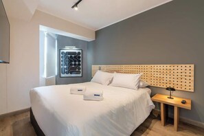 Moderni hotellihuone, jossa on suuri sänky, puinen pääty, yöpöytä lampulla ja seinälle asennettu taideteos.