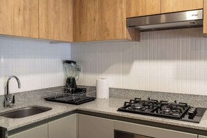 A kitchen with wooden cabinets, a stainless steel range hood, a sink, and a dish rack.