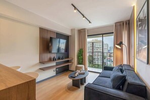 A modern living room with a flat-screen TV, a sofa, a coffee table, and a balcony with a view of the city.