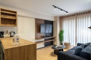 A modern living room with a wooden coffee table, a black sofa, a TV mounted on a wall, and a potted plant.