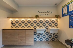 A bathroom with a geometric patterned wall, two sinks, a wooden cabinet, and a 'laundery room' sign.
