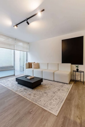 Ein modernes Wohnzimmer mit einem Ecksofa, einem Couchtisch, einem großen, schwarzen Kunstwerk und einem Blumentopf.