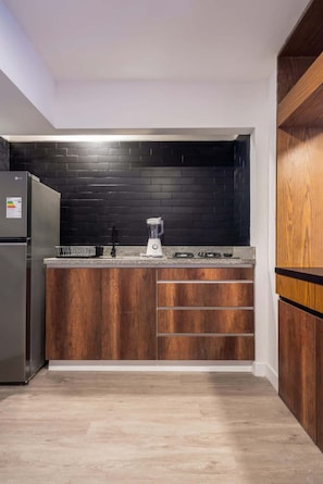 Eine kleine Küche mit dunkelholzartigen Schränken, einer schwarzen Spritzschutzwand und einem integrierten Kühlschrank.