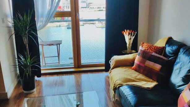 A modern living room with a glass coffee table, a leather sofa, a potted plant, and a view of a body of water through a large window. - Waterfront Views 2 Beds / 2 Baths (Dublin)