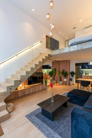 A modern interior with a staircase, a living area with a TV, and a kitchen.