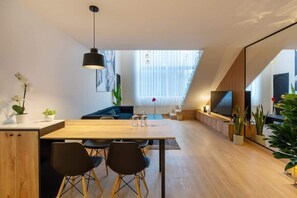 A modern living space with a dining area, a sofa, a TV, and plants.