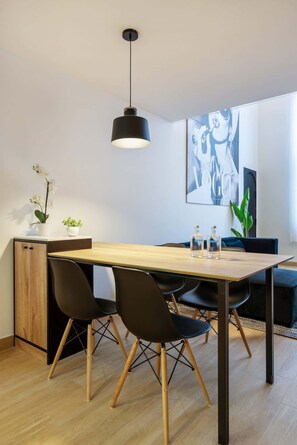 A modern dining area with a wooden table, black chairs, a pendant light, and a large framed artwork on the wall.