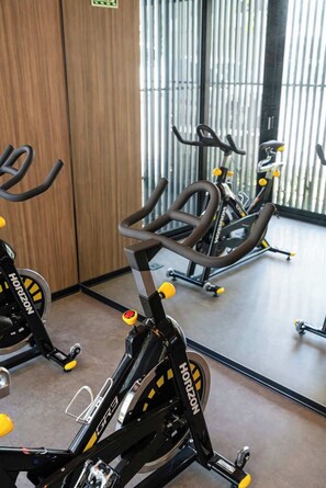 Ein Fitnessraum mit Ergometer, einer Holztür und einem großen Spiegel, der die Fahrräder reflektiert.