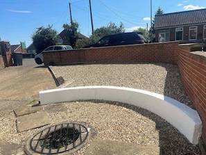 A parking area with a gravel surface, a white curved wall, and a metal grate. - Blyton 2-Bed Cottage, Parking, 30m to Lincoln (Blyton, Gainsborough)