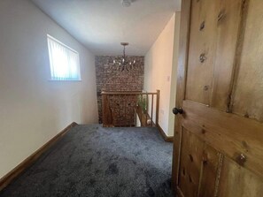 A room with a sloped ceiling, a stone accent wall, a wooden door, and a window with blinds. - Blyton 2-Bed Cottage, Parking, 30m to Lincoln (Blyton, Gainsborough)