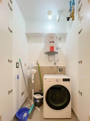 Un lavadero con lavadora, calentador de agua y utensilios de limpieza.