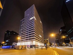 Un edificio de gran altura con varios pisos, ventanas iluminadas y una calle pavimentada al frente.
