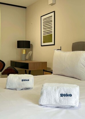 Habitación de hotel con una cama, un escritorio, una silla, una lámpara y un cuadro en la pared.
