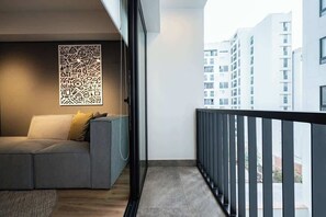 Un balcon avec un canapé gris et un panneau décoratif mural, donnant sur un paysage urbain.