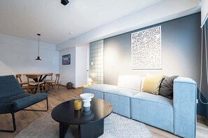 Un salon moderne comprenant un canapé, une table basse, une table à manger avec des chaises et un luminaire suspendu.