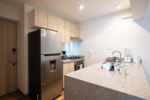Une cuisine moderne dotée d’un réfrigérateur en acier inoxydable, de meubles en bois, d’un plan de travail en granit, d’un four encastré et d’une machine à café.