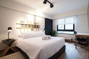 Une chambre d’hôtel moderne dotée d’un grand lit, d’un bureau, d’un ordinateur et d’une fenêtre donnant sur la ville.