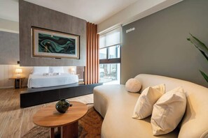 Ein modernes Hotelzimmer mit Bett, Sofa, Couchtisch, einem Gemälde und einem Fenster mit Vorhängen.