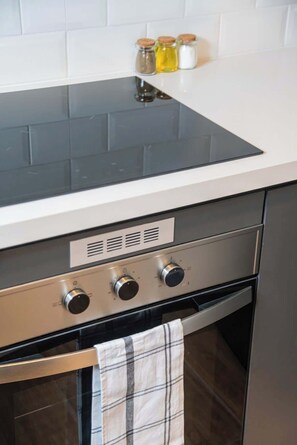 Eine Küche mit schwarzem Induktionskochfeld, einem Edelstahlbackofen und einer weißen Arbeitsplatte.