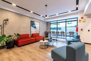 A modern lobby with a red sofa, a grey armchair, a round coffee table, and a large window with a view.