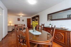 A dining area with a round table, chairs, a vase with flowers, a cabinet, and a mirror on the wall. - Geko | Outstanding 3BR near the Malecón (Miraflores)