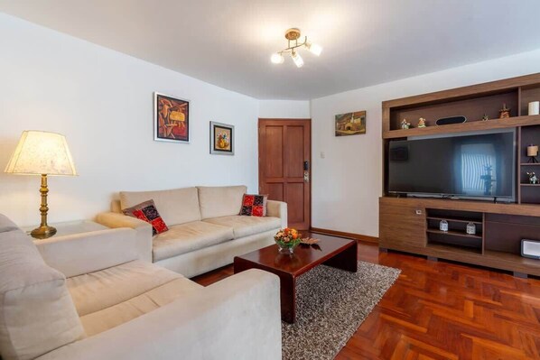 A living room with a sofa, coffee table, TV stand, and artwork on the walls. - Geko | Outstanding 3BR near the Malecón (Miraflores)