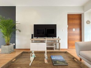 Ein modernes Wohnzimmer mit einem Flachbildfernseher, einem Holztisch, einer Couch und einer Topfpflanze.