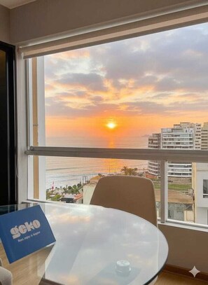 Ein Zimmer mit Blick auf den Sonnenuntergang über dem Meer, ein Tisch mit Glasplatte und ein Stuhl.