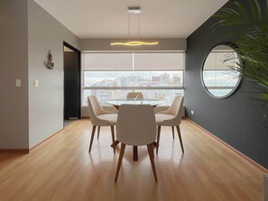 Ein modernes Interieur mit einem runden Tisch und Stühlen, großen Fenstern mit Stadtblick und einem runden Spiegel an der Wand.