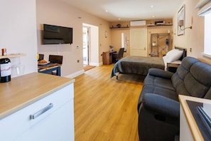 A room with a bed, a sofa, a desk, a TV, and a wooden floor.