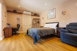 A bedroom with a bed, a desk, a chair, a sofa, and a wall-mounted shelf.
