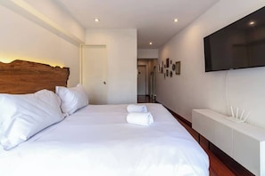 Ein Hotelzimmer mit einem großen Bett, einem Holz-Kopfteil, einem flachbildfernseher an der Wand und einem weißen Konsolentisch.