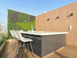 A rooftop bar with a wooden wall, a green wall with plants, and a seating area with chairs and a table.