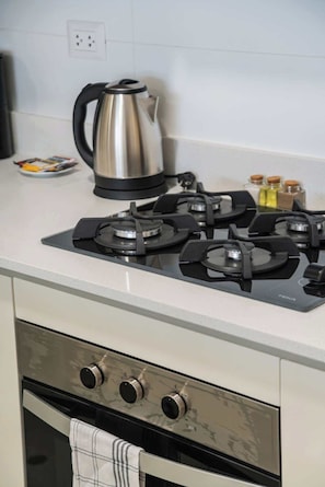A kitchen with a gas stove, a kettle, and a small plate with utensils.