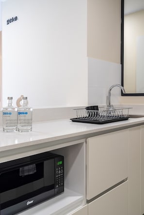 A kitchen with a microwave, sink, and two bottles of Geko water.