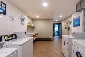 Un cuarto de lavandería con electrodomésticos blancos, un panel de control digital y carteles informativos en las paredes.