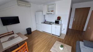 A compact kitchen with white cabinets, a microwave, and a small sink. There's a dining table with chairs and a TV mounted on the wall. - B studio with balcony, garden & sea view (Seget Vranjica)