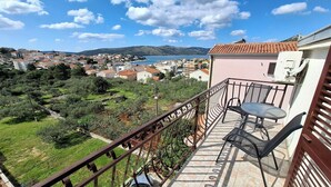 A balcony with a table and chairs overlooking a coastal town and sea. - B studio with balcony, garden & sea view (Seget Vranjica)