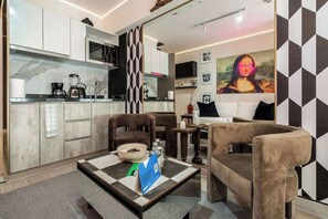 Una sala de estar moderna con un sofá, dos sillones, una mesa de centro y una zona de cocina con electrodomésticos.