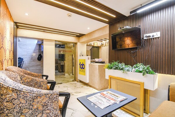 A hotel reception area with a reception desk, a clock, and a seating area with patterned sofas. - Fabhotel Aayash (Bidhannagar)