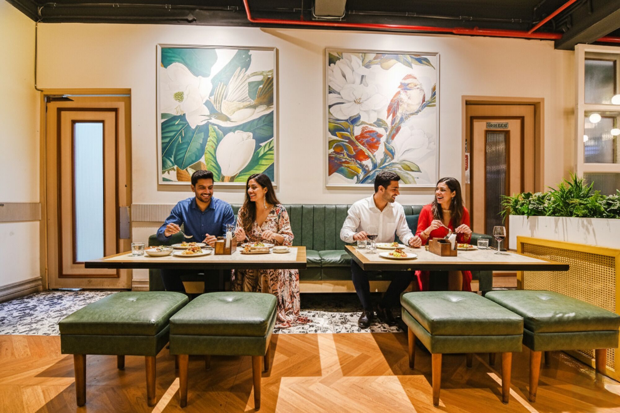 A dining area with wooden tables and green cushioned benches, surrounded by large floral paintings on the walls.