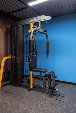 Ein Fitnessraum mit Langhantelbank, Squat-Gestell und Kabelzug vor blauer Wand.