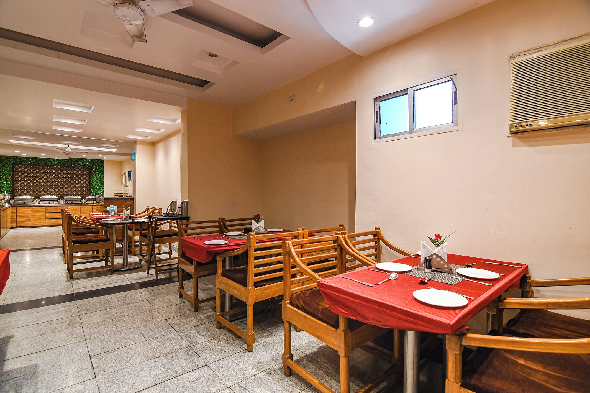 Un comedor con mesas y sillas de madera, una barra de buffet y un ventanal con persianas.