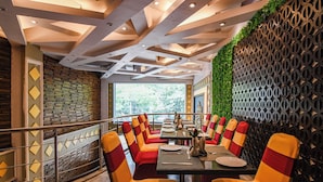 A restaurant with a modern interior, featuring a long table with chairs, a decorative wall, and a view of greenery outside.